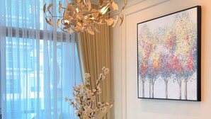 Een eetruimte met een marmeren tafel, vier stoelen, een roze vaas met bloemen, een moderne kroonluchter en een kleurrijk abstract schilderij aan de muur.
