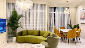 Een woonkamer met een groene bank, gele stoelen, een eettafel en een televisie aan de muur.