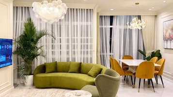 A living room with a green sofa, yellow chairs, a dining table, and a TV on the wall.