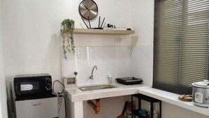 Una cocina compacta con un lavamanos, un microondas, un reloj y una ventana con persianas.
