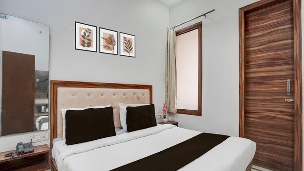 A hotel room with a bed, a wooden wardrobe, a mirror, and three framed pictures on the wall. - Super Collection O Townhall Heritage Complex (Amritsar)