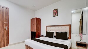 A bedroom with a wooden wardrobe, a bed with a tufted headboard, a bedside table, and a mirror. - Super Collection O Townhall Heritage Complex (Amritsar)