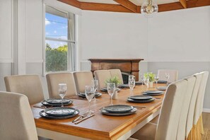 Une salle à manger avec une table en bois dressée pour six personnes, des chaises de couleur beige et une cheminée en arrière-plan.