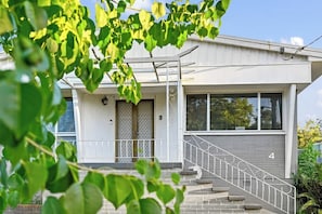 Une maison moderne à deux étages, avec une façade grise, un numéro « 4 » bien visible sur le devant, et un escalier menant à l’entrée.