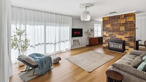 A modern living room with a fireplace, a television, and a sofa. - Seednest Blue Lake King Bed & BBQ Backyard (Mount Gambier)