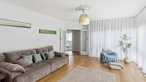 A living room with a sofa, a rug, a plant, and a ceiling light. - Seednest Blue Lake King Bed & BBQ Backyard (Mount Gambier)