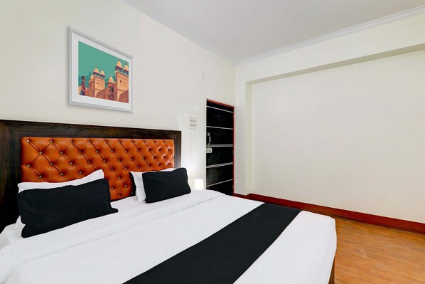 A hotel room with a large bed, a headboard, a framed picture on the wall, and a wardrobe.