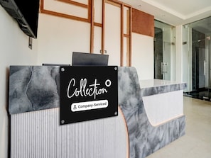 Un mostrador de recepción con encimera de mármol, un letrero negro que dice 'Collection' y 'Company-Serviced', y una puerta de vidrio al fondo.