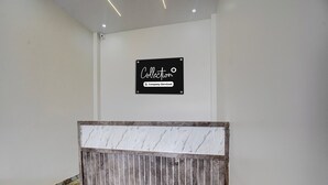 Zona de recepción de un hotel con piso estampado en mármol, un mostrador de recepción con estructura metálica y un cartel que indica 'Collection Company-Serviced'.