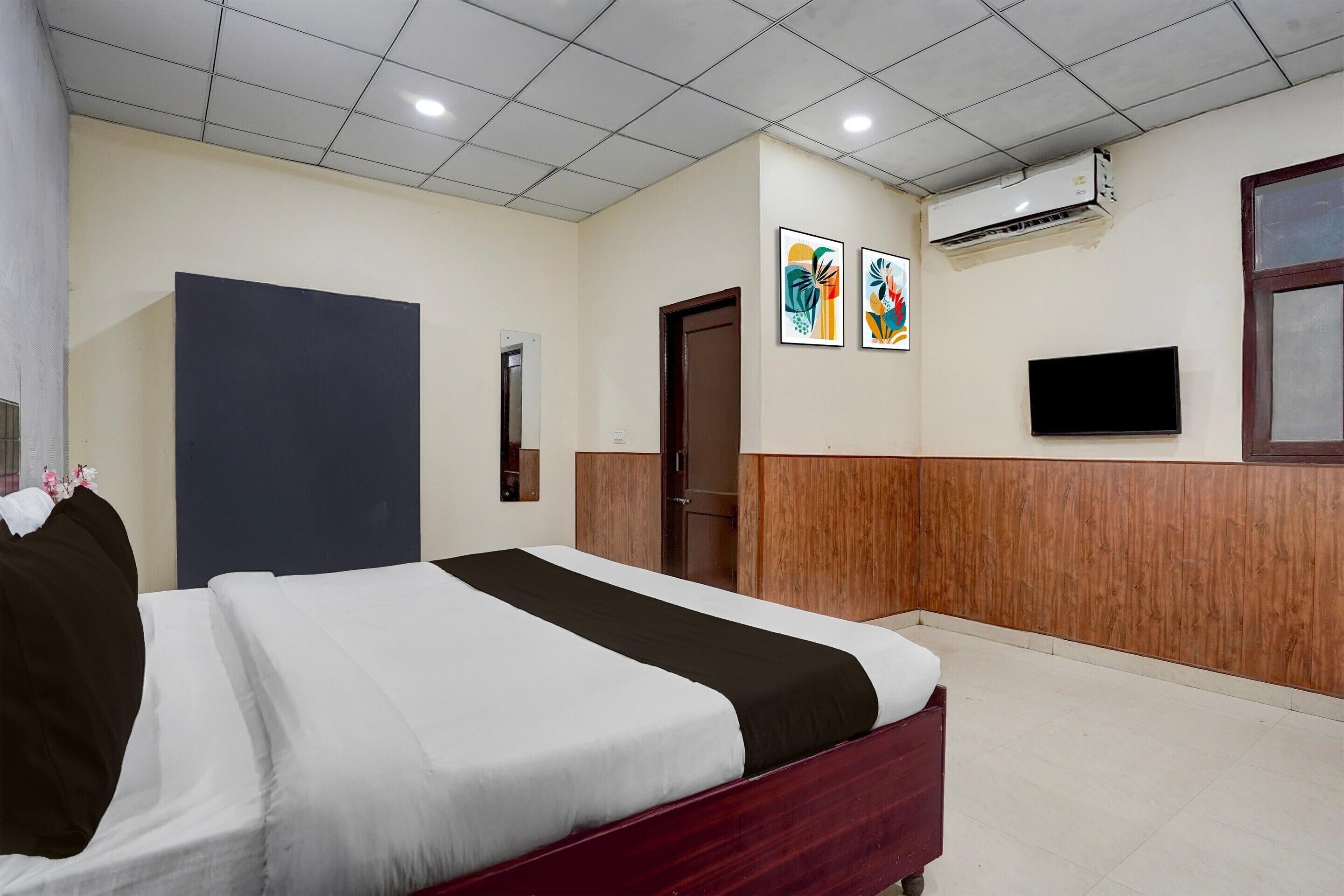 A hotel room with a bed, a television, an air conditioning unit, and a door.