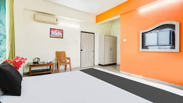 Une chambre d’hôtel comprenant un lit, un bureau avec une chaise, un appareil de climatisation, un tableau encadré et un mur d’accent de couleur orange.
