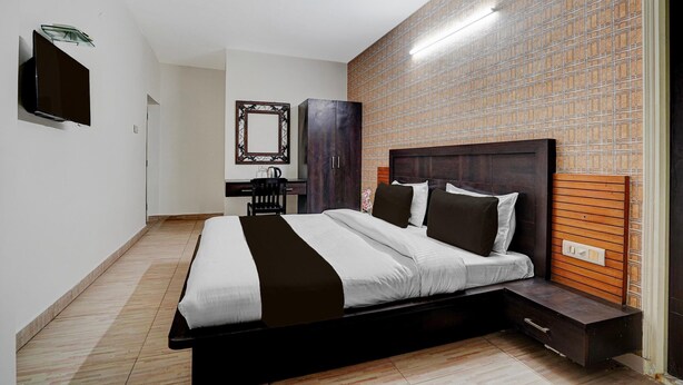 A bedroom with a bed, a TV, a desk, and a mirror.
