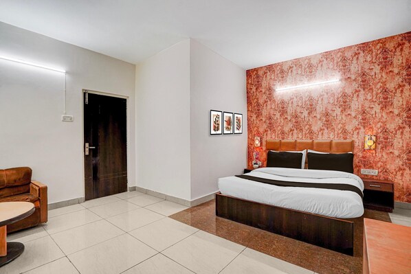 A hotel room with a bed, a wooden bench, a door, and a wall with patterned wallpaper.