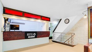 A hotel reception desk with a sign, a clock, and a staircase.