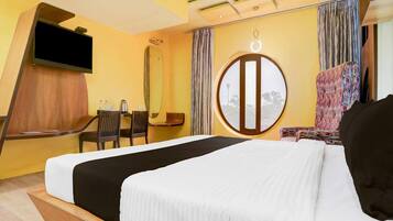 A hotel room with a bed, a desk with a chair, a television, a round window, and a mirror.
