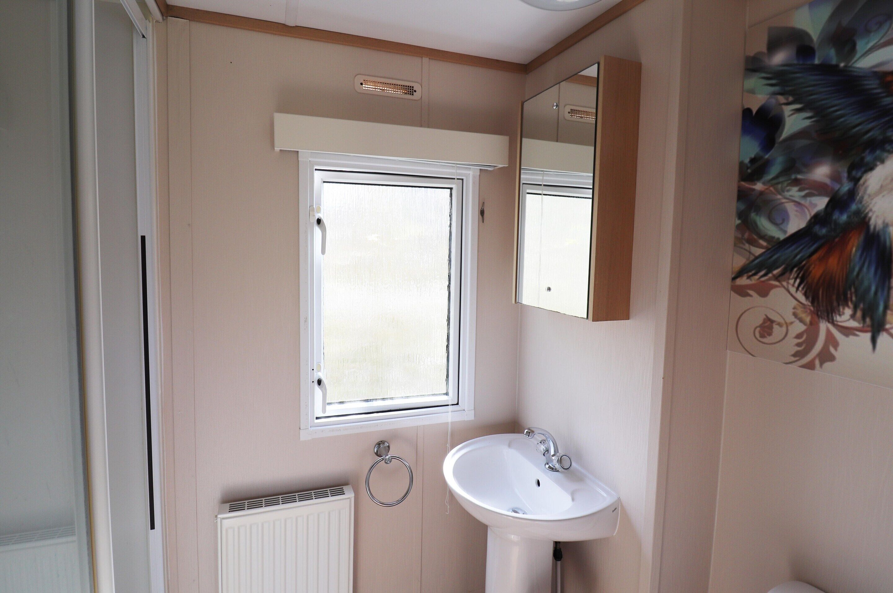 Ein Badezimmer mit Fenster, Waschbecken, Handtuchhalter und Heizkörper.