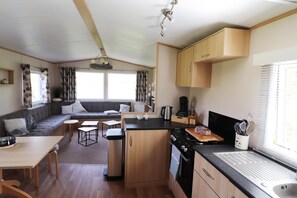 A compact kitchen with a stove, sink, and a dining area with a sofa and table. - Cozy Chalet With a View Over the Fields (Drachten)