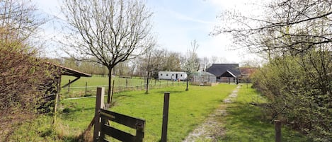A rural landscape with a grassy field, a wooden bench, a fenced area, and a small building in the distance.