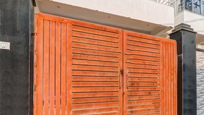 A double wooden gate with horizontal slats, a black pillar, and a white wall with a window. - Classic With Balconybhu IIT Mahamanpuri BLW (Varanasi)