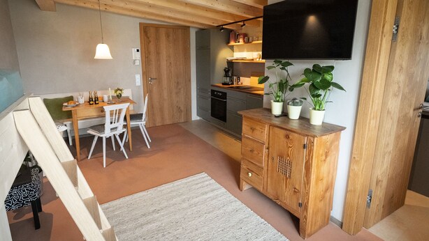 Una cocina moderna con armarios de madera, un comedor con mesa y sillas, y un televisor de pantalla plana montado en la pared.