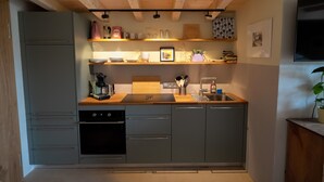 Una cocina moderna con armarios grises, encimeras de madera, horno empotrado y un fregadero. Hay estantes sobre la encimera con diversos utensilios de cocina.