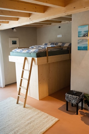 Un lit superposé avec une échelle, une petite table avec une figurine de souris et un tableau accroché au mur.