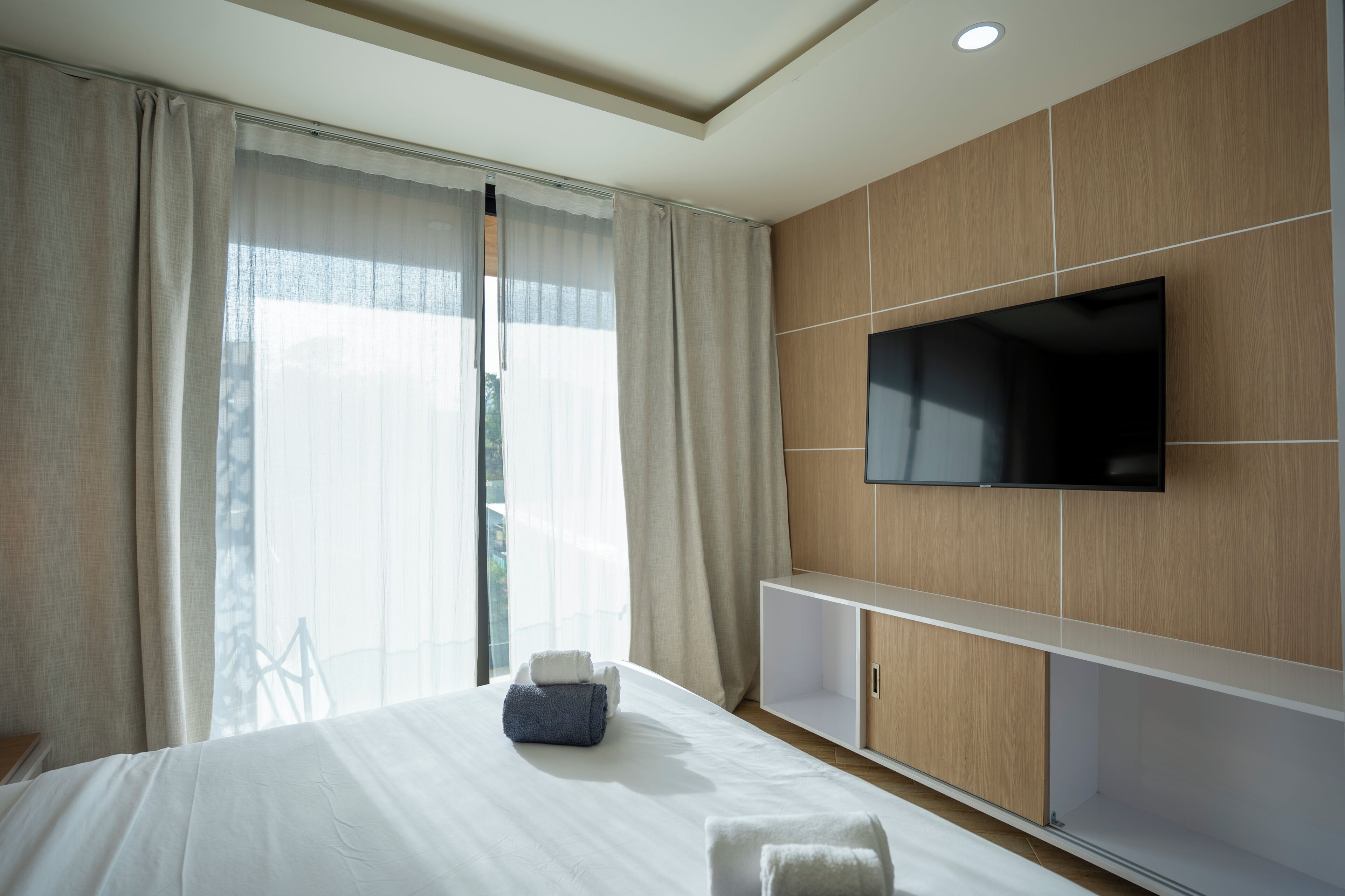 Une chambre d’hôtel avec un lit, un téléviseur fixé au mur et une grande fenêtre avec des rideaux.