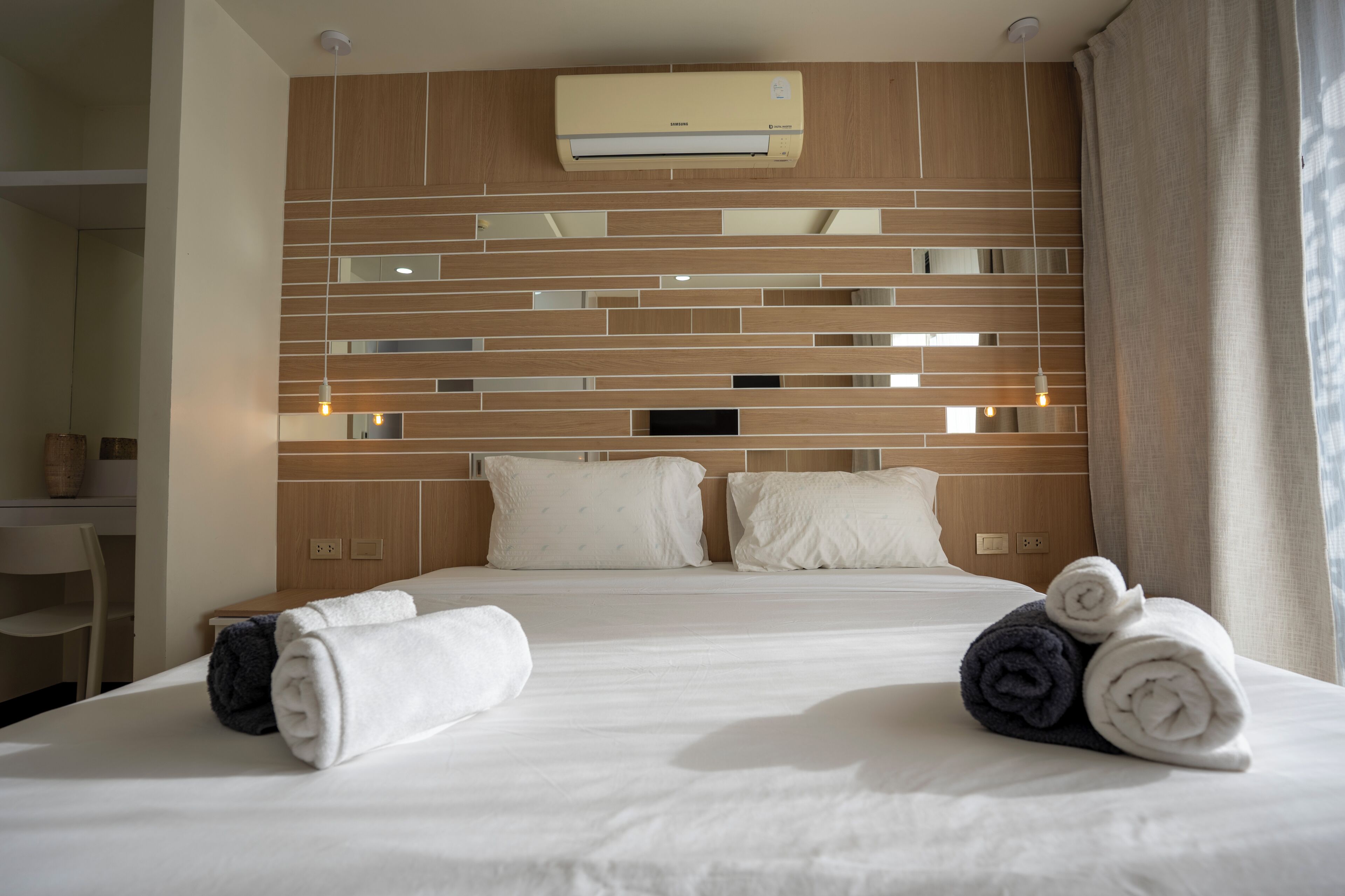 Een hotelkamer met een bed, kussens, een nachtkastje, een airconditioner en een spiegel.