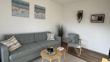 A modern living room with a grey sofa, two armchairs, a coffee table, and a bookshelf.