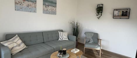 A modern living room with a grey sofa, two armchairs, a coffee table, and a bookshelf.