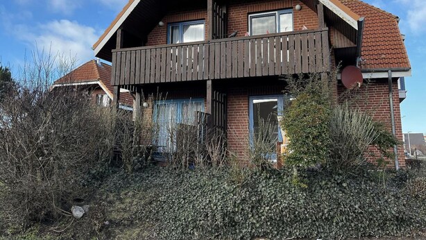 Et toetagers hus med balkon, omgivet af tæt buskads.