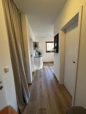 A narrow hallway with a kitchen area at the end, featuring cabinets, a countertop, and a window. - Ferienwohnung in Lemkenhafen auf Fehmarn (Fehmarn)