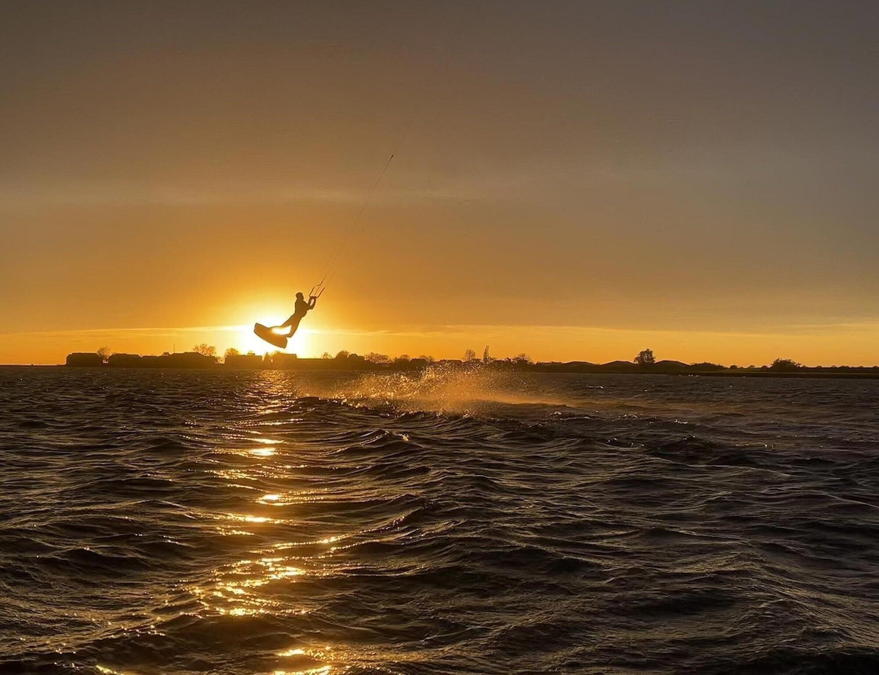 A person kite surfing at sunset with a silhouette of buildings in the background.