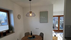 Spiseområde med et træbord, stole, en hængende lampe, et ur og et indramet citat på væggen.