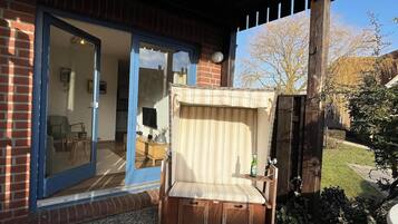 A wooden bench with a cushioned seat and backrest, positioned outside a building with a glass door and a brick wall.