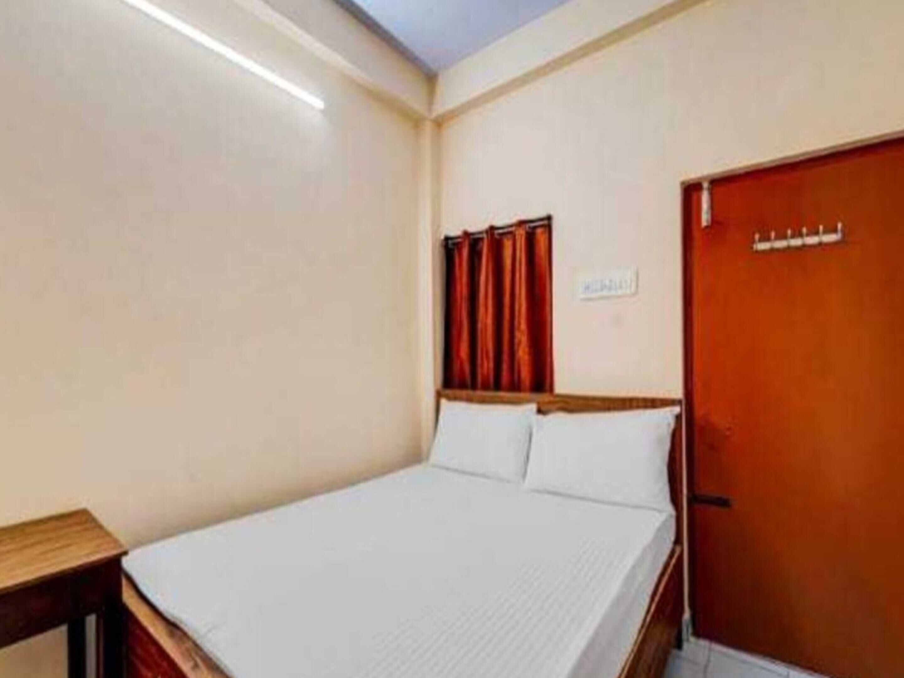 A hotel room with a bed, a wooden nightstand, a door, and a light fixture on the ceiling.