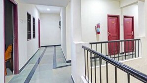 A hallway with a marble floor, red doors, and a fire extinguisher.