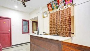 A reception desk with a patterned backdrop, a ceiling fan, and a red door. - Collection O Gummidipundi Bus Terminal (Gummidipundi)