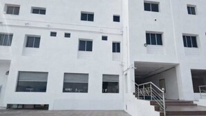 A white multi-story building with a flat roof, large windows, and a covered entrance with stairs. - Collection O Gummidipundi Bus Terminal (Gummidipundi)