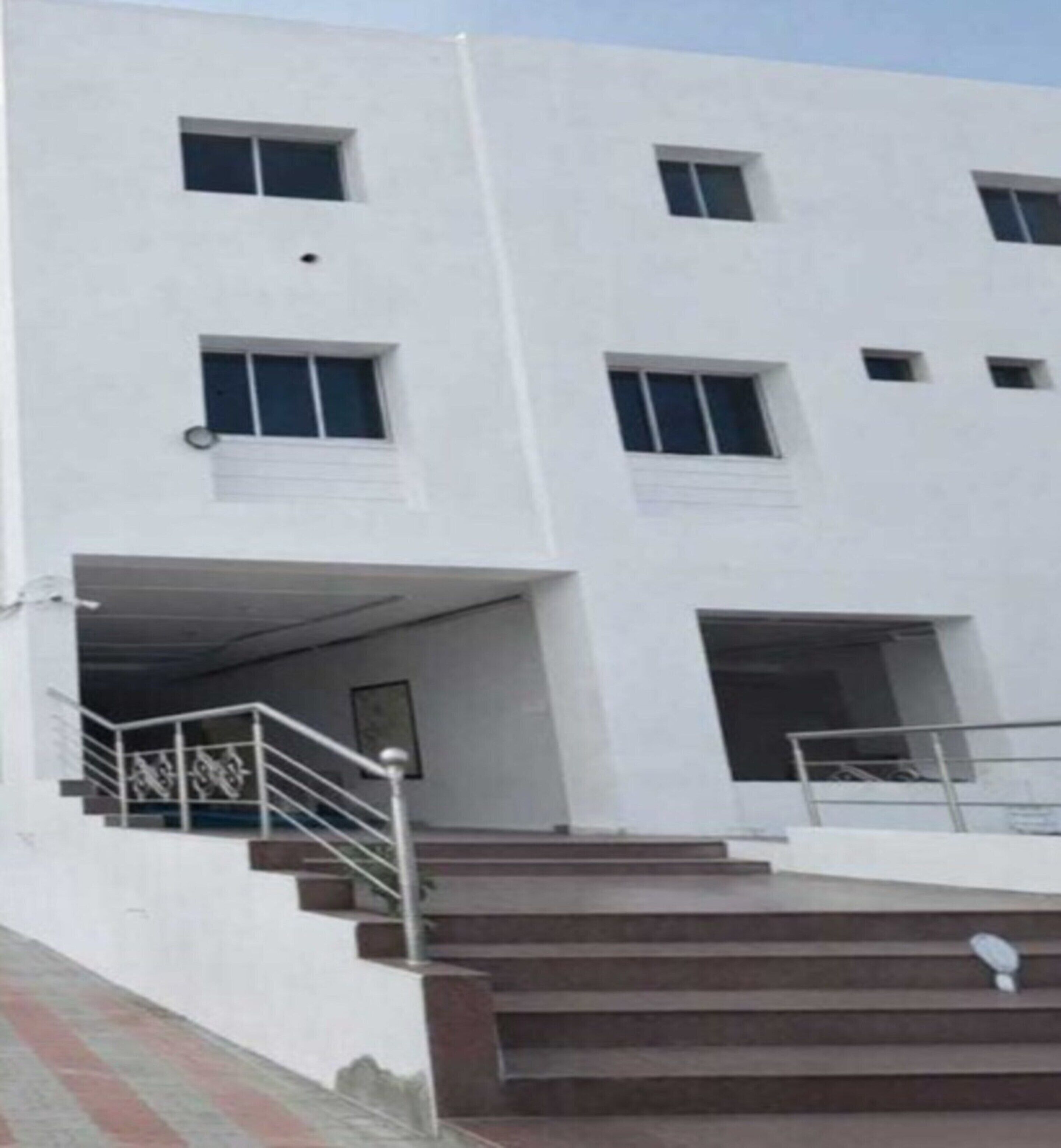A multi-story building with a white facade, several windows, and a set of stairs leading to an entrance.