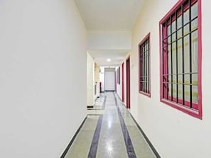 Un pasillo con suelo de baldosas, paredes blancas y ventanas con marcos rojos.