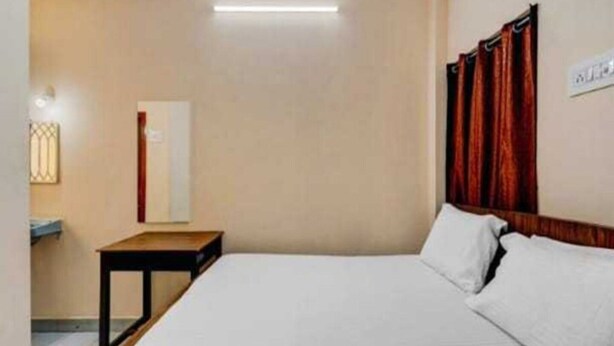 A hotel room with a bed, a nightstand, a wall-mounted light, and a window with curtains. - Collection O Gummidipundi Bus Terminal (Gummidipundi)