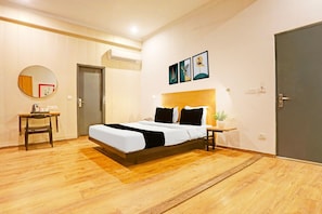 A modern bedroom with a wooden floor, a bed with white bedding, a bedside table with a lamp, a round mirror, and a door.