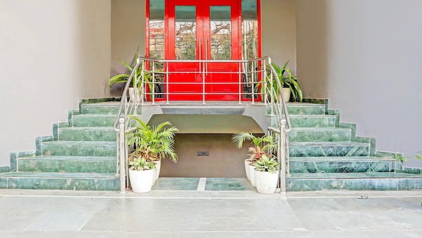 Una escalera con una puerta roja en la parte superior, plantas en macetas abajo y una barandilla de metal.