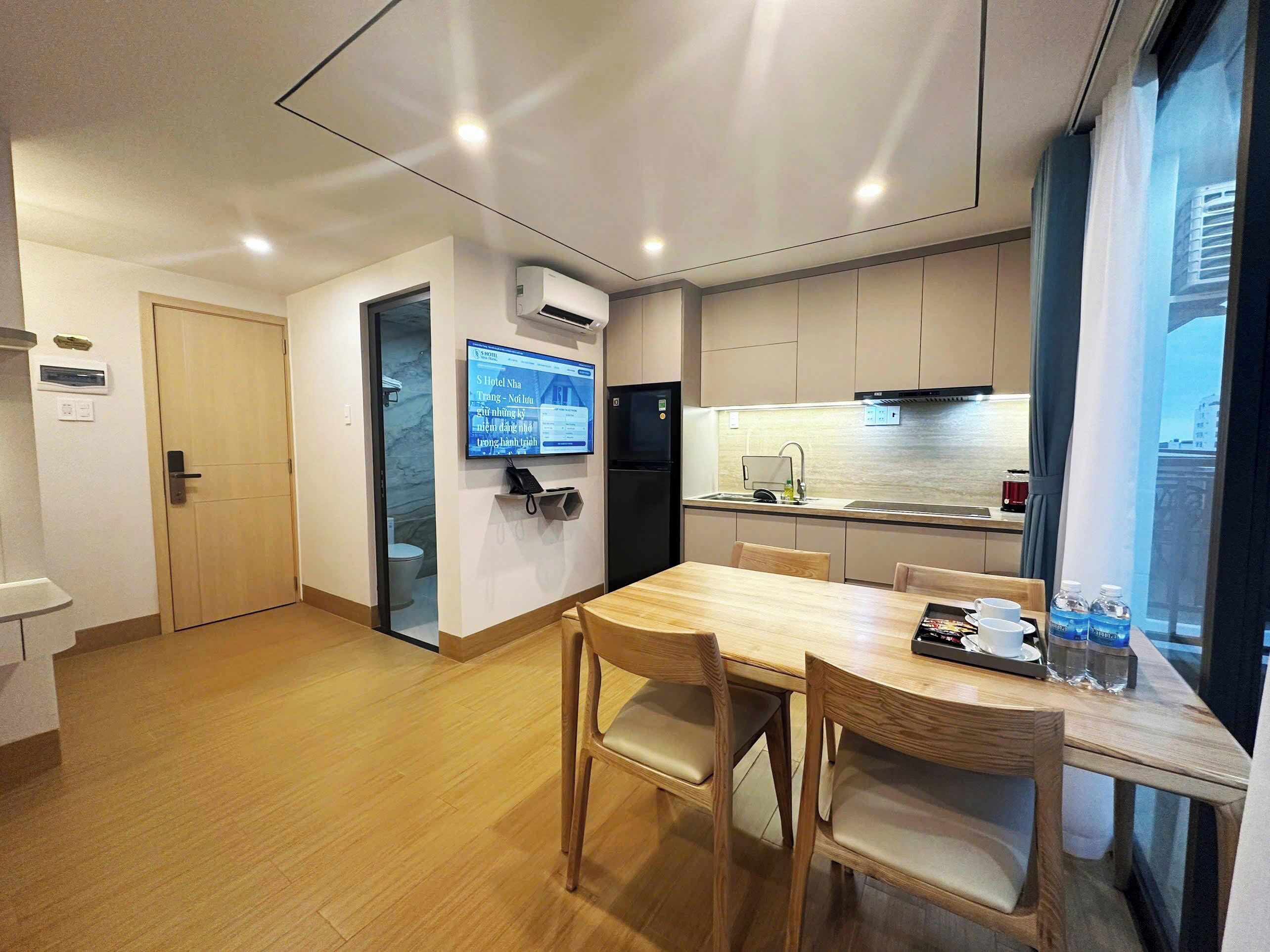 A modern kitchen with a built-in oven, a refrigerator, and a sink. There is a dining area with a wooden table and chairs.
