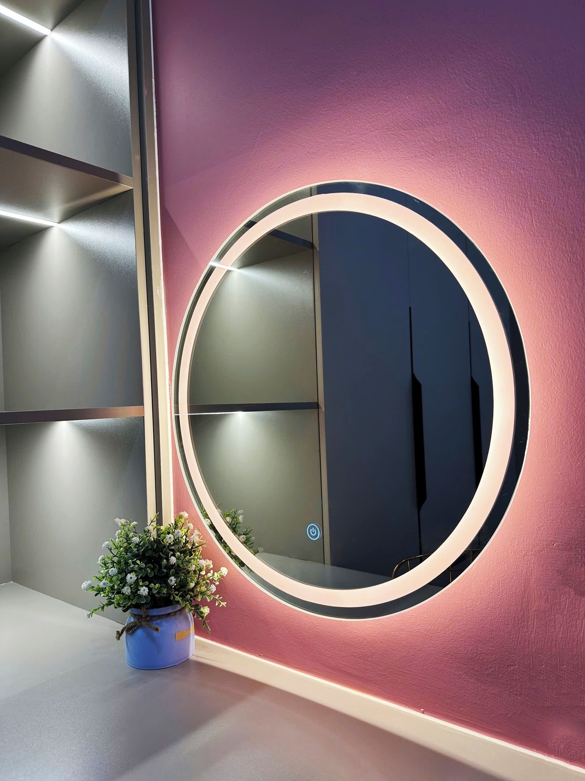 A circular mirror with a power button, a potted plant, and a modern wall design.