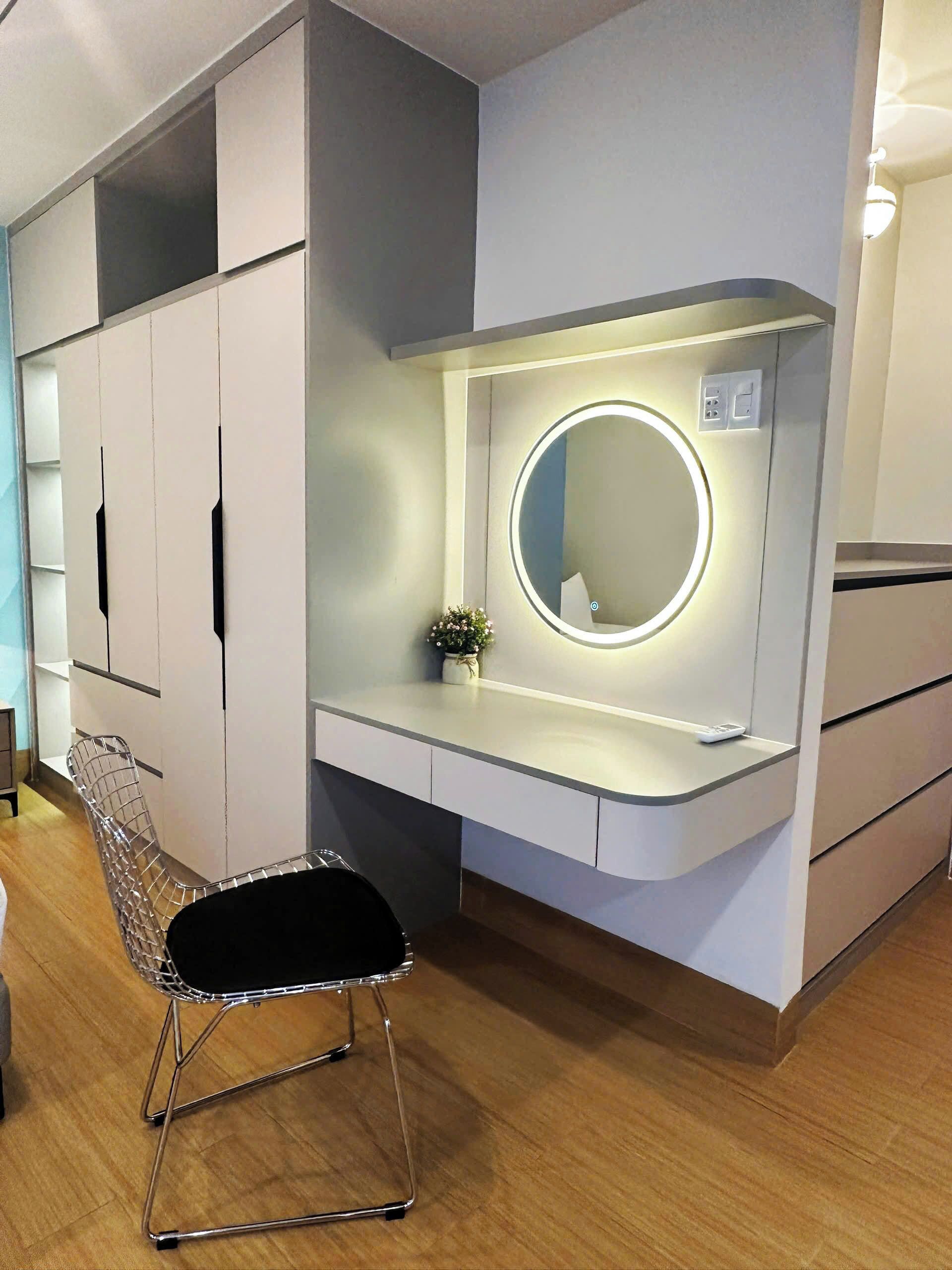 Une chambre moderne dotée d’un coin coiffeuse, d’un miroir rond avec éclairage intégré, d’une chaise et d’armoires de rangement encastrées.