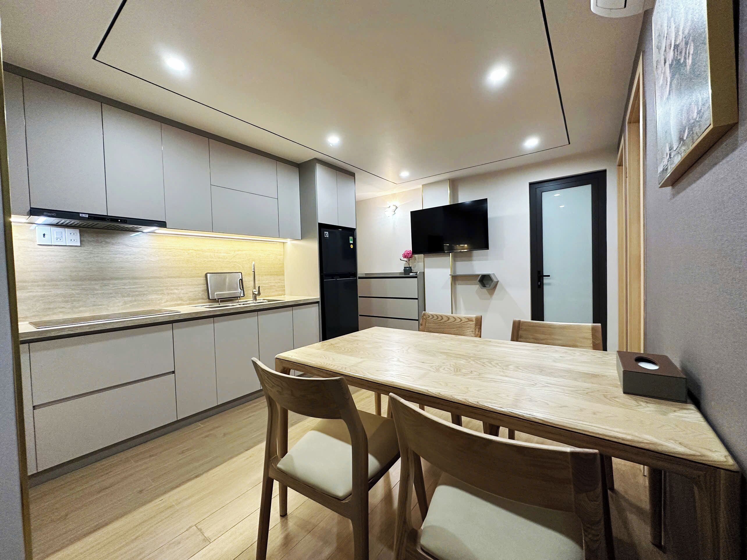 A modern kitchen with a dining area, equipped with a refrigerator, stove, and a flat-screen TV.