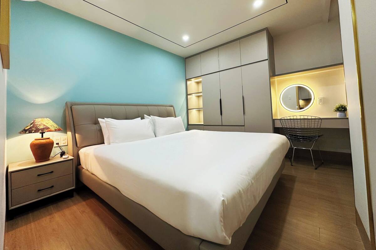 Un dormitorio moderno con cama, mesita de noche, lámpara y escritorio con silla y espejo.
