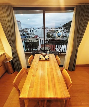 Un balcon avec une table et des chaises en bois, une poubelle et une vue sur les immebles.
